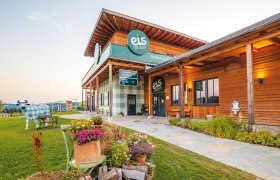 Gebäude von Eis Greissler mit Holzfassade und dekorativer Kuhfigur im Garten.