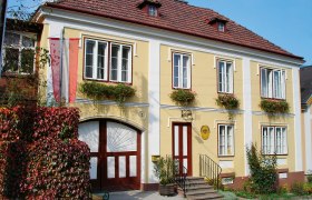 Historisches gelbes Gebäude mit roten Fensterläden und Blumen, beschriftet als Kaiserpostamt.