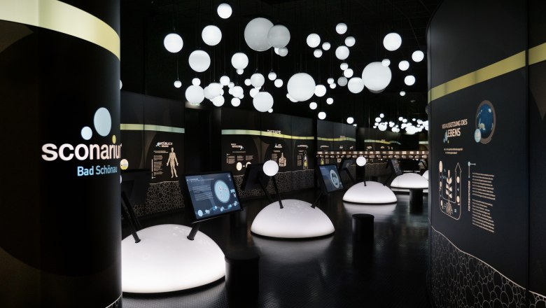 Innenansicht einer modernen Ausstellung mit beleuchteten Kugeln und interaktiven Displays.