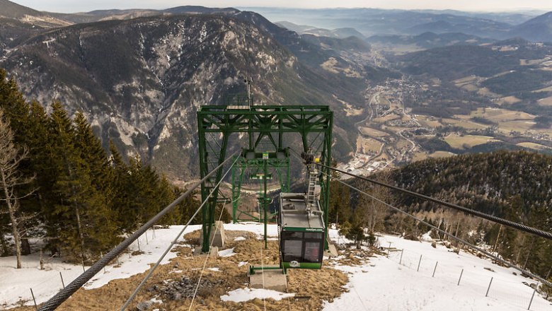 Die Raxseilbahn schwebt majest&auml;tisch &uuml;ber die schneebedeckten H&auml;nge, w&auml;hrend die atemberaubende Berglandschaft sich unter ihr entfaltet. Hier, wo die frische Bergluft und die Ruhe der Natur aufeinandertreffen, wird jeder Moment zu einem unvergesslichen Erlebnis. Genie&szlig;en Sie die spektakul&auml;ren Ausblicke und die unber&uuml;hrte Sch&ouml;nheit der Alpen.