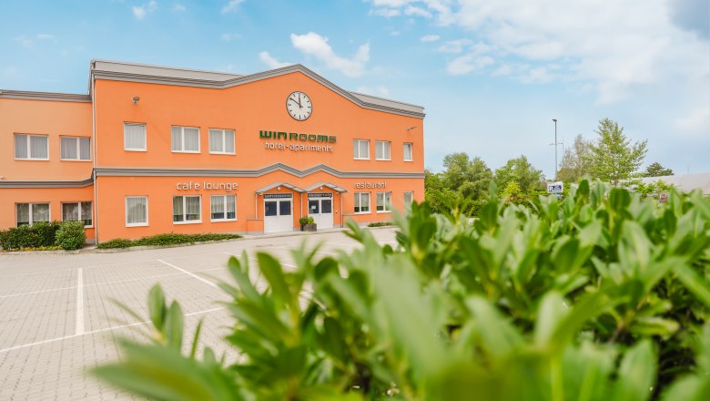 Au&szlig;enansicht eines orangefarbenen Geb&auml;udes mit der Aufschrift 'Win Rooms hotel-apartments'.