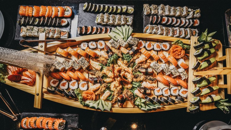 Ein großes Sushi-Buffet auf einem Holztablett mit verschiedenen Sushi-Varianten, dekoriert mit Gurken und Ingwer.